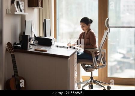 Una donna indiana seria si siede alla scrivania e tiene le informazioni di jotting della penna Foto Stock