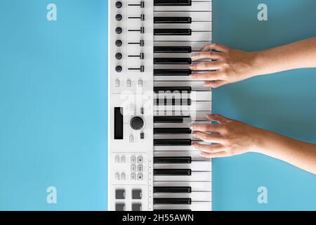 Le mani femminili suonano i tasti musicali su sfondo blu, vista dall'alto. Foto Stock