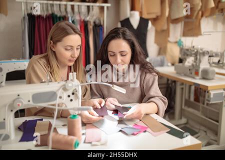 Due giovani comò o colleghi di stilista che lavorano e discutono di designer di progetto di moda e guardare attraverso i campioni di tessuto per i vestiti, professione Foto Stock