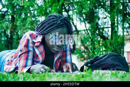 Ragazza adolescente africana sdraiata sull'erba facendo lezione di scuola. Concetto di happyness e di highteartedness. Foto Stock