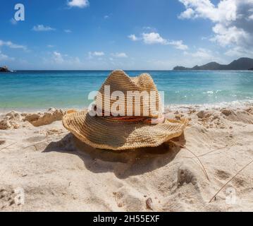 Accessori da spiaggia con cappello di paglia sulla spiaggia sabbiosa tropicale e sul mare blu Foto Stock