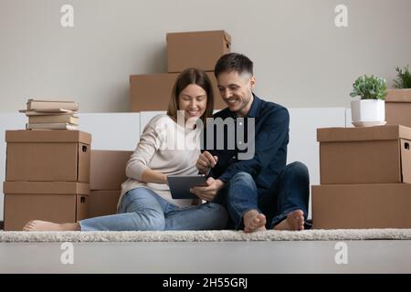 Coppia felice usando il tablet, seduto sul pavimento in una nuova casa Foto Stock