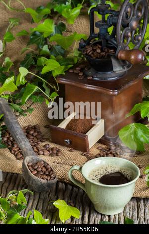 Un macinacaffè con macine e chicchi di caffè. Una tazza di caffè appena fatto. fotografia da studio Foto Stock