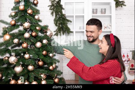 Felice coppia sposata sta decorando un albero di Natale alla vigilia di Natale. Foto Stock