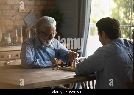 Vecchio padre entusiasta giocare amichevole scacchi partita con figlio grownup Foto Stock