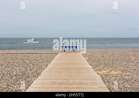 Panca pubblica blu, di fronte al mare, alla fine di un ponte pedonale in legno sulla spiaggia di ciottoli di Tréport, Francia Foto Stock