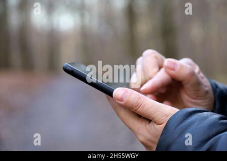 Mani femminili con smartphone in primo piano su sfondo sfocato del parco autunnale. Donna che usa il telefono cellulare all'aperto in climi freddi Foto Stock