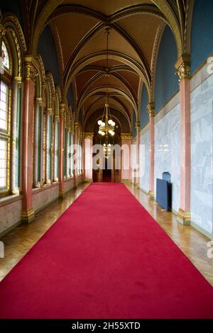 BUDAPEST, UNGHERIA - 03 MAR 2019: Lungo corridoio con tappeto rosso su pavimento in marmo e lampadario sul soffitto nell'edificio del Parlamento ungherese Foto Stock