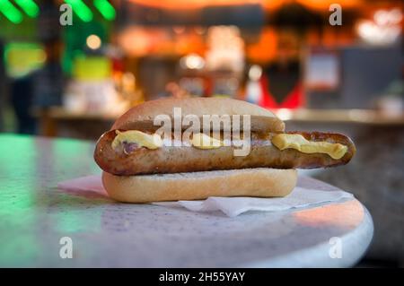 Salsiccia di bratwurst con senape in una pistola, fast food tipico al carnevale tedesco viaggiante, buon divertimento e mercatino di Natale, luci sfocate di notte, copia Foto Stock