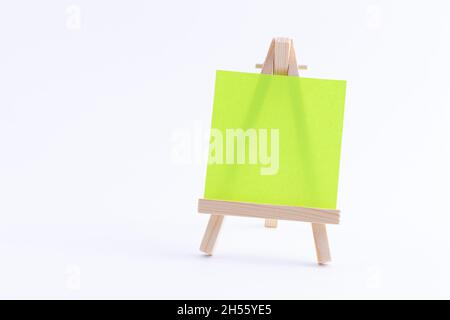 Easel in legno in miniatura con tela quadrata colorata vuota o carta Memo - Mockup. Mini supporto in legno con tavola da disegno pulita su sfondo bianco, spazio per la copia Foto Stock