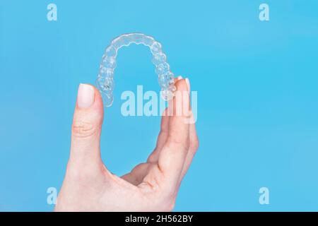 Regge a mano rimovibile invisibile trasparente allineatore invisibile invisalign o in plastica reggiseni ortodontici su sfondo blu Foto Stock