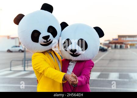 Immagine narrativa di una coppia che indossa una testa panda gigante e abiti colorati. Uomo e donna che fanno festa in un parcheggio. Foto Stock