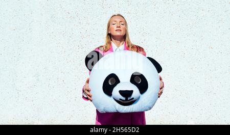 Immagine narrativa di una coppia che indossa una testa panda gigante e abiti colorati. Uomo e donna che fanno festa in un parcheggio. Foto Stock