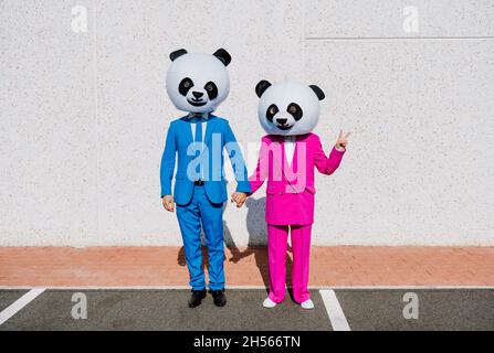 Immagine narrativa di una coppia che indossa una testa panda gigante e abiti colorati. Uomo e donna che fanno festa in un parcheggio. Foto Stock