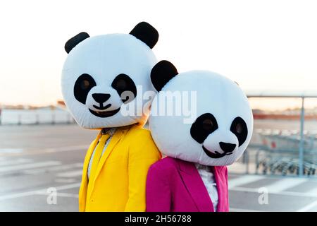 Immagine narrativa di una coppia che indossa una testa panda gigante e abiti colorati. Uomo e donna che fanno festa in un parcheggio. Foto Stock