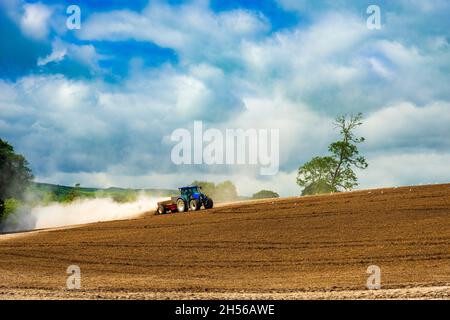 Una nube di polvere si espande dietro un trattore che aratura un campo Foto Stock