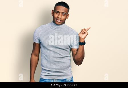 Giovane uomo nero che indossa una t shirt casual con un grande sorriso sul viso, puntando con il dito della mano verso il lato guardando la fotocamera. Foto Stock