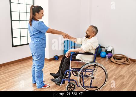 Uomo anziano seduto su sedia a rotelle e infermiera geriatrica che fa accordo di scuotimento della mano, ringraziando per l'aiuto Foto Stock