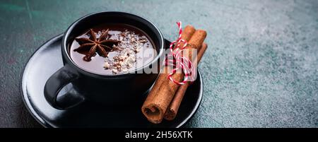 Cioccolata calda con anice e noci in tazza di ceramica nera su vecchio sfondo verde scuro di cemento. Messa a fuoco selettiva. Foto Stock