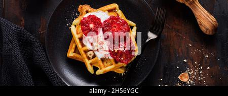 Waffle con yogurt e salsa rossa d'arancia siciliana su vecchio sfondo di legno scuro. Vista dall'alto. Foto Stock