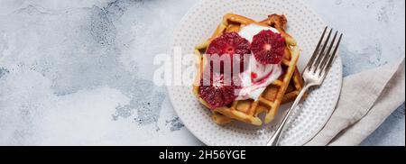 Waffle con salse allo yogurt e salse rosse d'arancia siciliana su sfondo vecchio chiaro. Vista dall'alto. Foto Stock