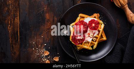 Waffle con yogurt e salsa rossa d'arancia siciliana su vecchio sfondo di legno scuro. Vista dall'alto. Foto Stock