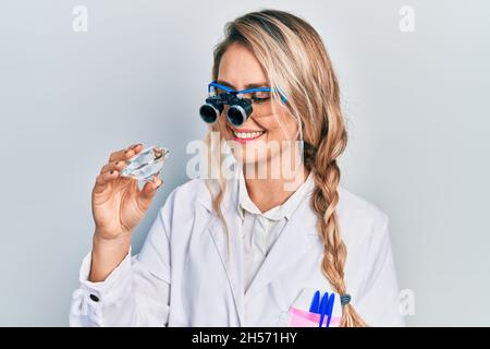 Bella giovane donna bionda che tiene brillante diamante pietra indossare occhiali lente di ingrandimento sorridente con un sorriso felice e fresco sul viso. Mostrando denti. Foto Stock