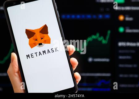 Ucraina, Odessa - Ottobre, 9 2021: Tenere la mano mobile con l'app MetaMask in esecuzione sullo schermo dello smartphone con il trading cartellone a lume di candela sullo sfondo. Io Foto Stock