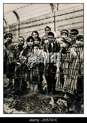 AUSCHWITZ BAMBINI AUSCHWITZ 1945 BAMBINI PRIGIONIERI LIBERAZIONE i bambini prigionieri che indossano uniformi a strisce stare fuori ai loro liberatori da dietro una recinzione di filo spinato nel famigerato campo di sterminio nazista della seconda Guerra Mondiale Auschwitz Polonia meridionale. Seconda guerra mondiale la seconda guerra mondiale si erge tranquillamente senza emozioni dietro la recinzione spinato di filo al campo di concentramento della seconda Guerra Mondiale di Germania nazista Auschwitz Birkenau Polonia. 1945 liberazione russa Foto Stock