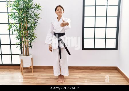 Giovane ispanica ragazza che indossa kimono karate e cintura nera sorridente amichevole offrendo handshake come saluto e accogliente. Business di successo. Foto Stock