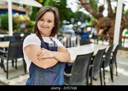 Giovane giù sindrome donna sorridente sicuro indossare grembiule al bar terrazza Foto Stock