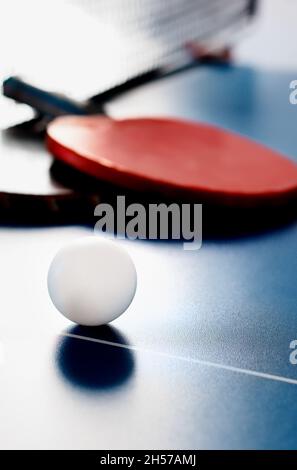 Due racchette da tennis e una palla bianca si trovano su un tavolo da tennis vicino alla rete. Attività ricreative attive e giocare a ping pong. Background sportivo. Foto Stock