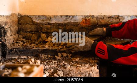 L'uomo distrugge una vecchia stufa di mattoni, mattoni neri in fuliggine, smantellando la vecchia cucina surface. Nuovo Foto Stock