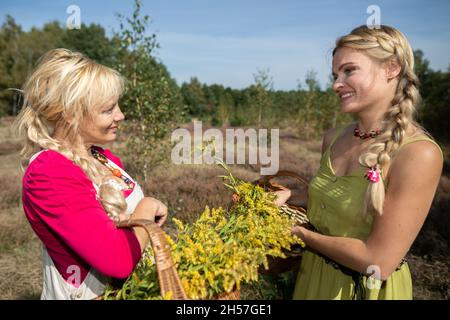 Due erboristi in piedi in un prato che gossiping dolcemente. Cesti pieni di erbe di goldenrod. Foto Stock