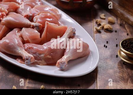 Pollo crudo biriyani tagliato senza pelle disposto su stoviglie bianche con ingredienti posti sullo sfondo con fondo rustico in legno. Foto Stock