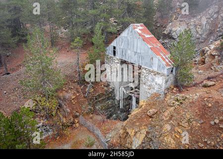 Miniera di cromite abbandonata nei monti Troodos, Cipro. Vecchio ascensore rotto su albero verticale circondato da pini Foto Stock
