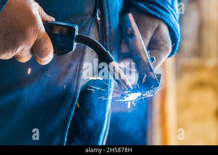 Primo piano di lavori di saldatura e di metallo nelle mani di un saldatore industriale. Foto Stock