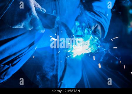 Primo piano di saldatura e lavorazione dei metalli nelle mani di una saldatrice industriale. Foto Stock