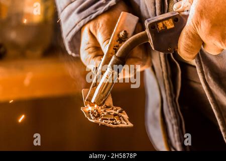 Le mani di una saldatrice maschio sono impegnate in lavori di saldatura e metallo, primo piano. Foto Stock