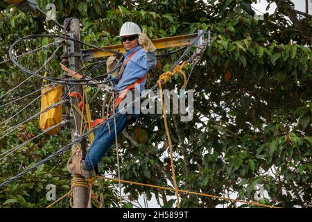 Elettricista maschio che lavora all'altezza di un palo luminoso. Lavoratore elettrico. L'elettricista si accende con i pollici. Foto Stock