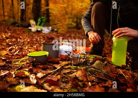 La donna usa un riscaldatore a gas portatile e una padella per cucinare all'aperto Foto Stock