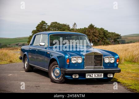 Rolls-Royce Silver Shadow parcheggiato su un vicolo di campagna con campi, brughiera e uno stand di alberi dietro Foto Stock