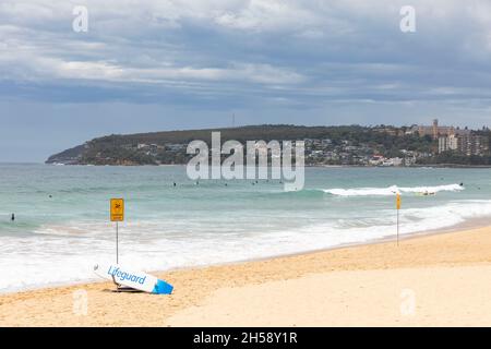 Bagnino surf surf Surfboard accanto a un pericoloso segnale di corrente d'acqua su Manly Beach a Sydney in un giorno di primavera, Sydney, Australia Foto Stock