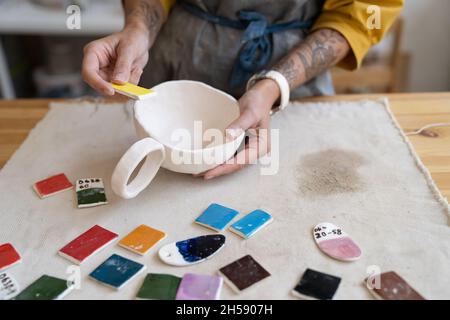 Ceramista di lavoro: Vasaio femminile che sceglie il colore per la pittura di tazza dalla tavolozza in studio, primo piano Foto Stock