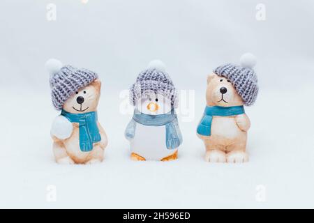 Figurine decorative a tema natalizio. La statuetta di un gatto, un pinguino e un orso in un cappello a maglia su sfondo bianco. Arredamento festivo. Foto Stock