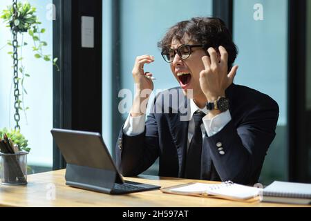 Un lavoratore di ufficio troppo lavorato è frustrato. Uomo d'affari stanco con molti lavori. Il manager ha sottolineato il fastidio dei dati finanziari sul tablet. Foto Stock