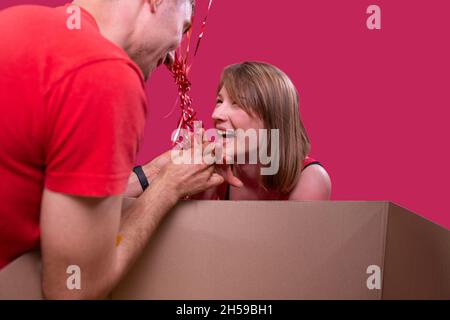 Primo piano foto di una giovane ragazza bionda sorridente e di un uomo in t-shirt rad mettendo l'anello sul suo dito ragazza, ha accettato il matrimonio Foto Stock