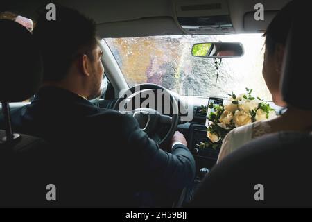 Interno vista del sedile anteriore sposa e sposo sedersi in auto mentre gli amici spruzzano vino frizzante su auto . Cultura e matrimoni in Lituania Foto Stock
