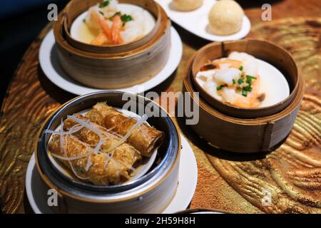 Piatti assortiti di dim sum fritto e cotto a vapore o gnocchi cinesi, serviti in cuci di bambù su un tavolo di legno in un ristorante cinese. Foto Stock