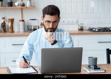 Serio uomo d'affari caucasico adulto che lavora in linea usando il laptop all'ufficio domestico Foto Stock